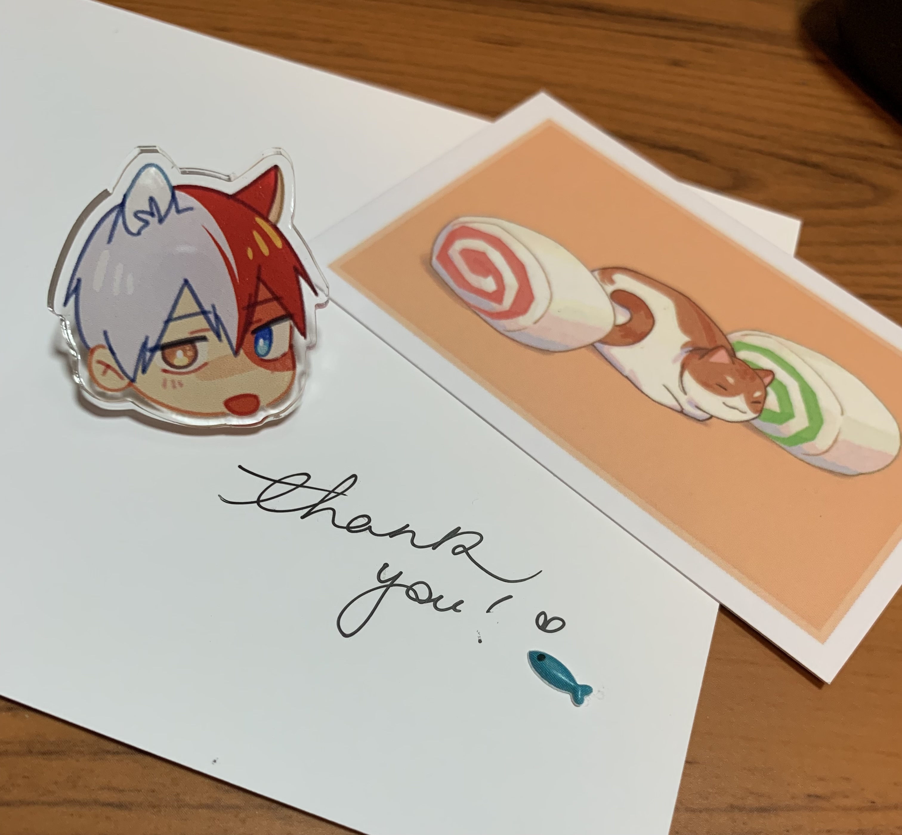 my photo of a cat todoroki blep pin from boku no hero academia, drawn by thatmightyheart from tumblr/twitter, along with a card that says 'thank you!' with a little heart and fish next to it and another card with a cat between two swiss roll cakes